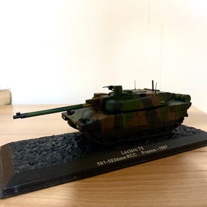 May include: A model Leclerc T5 tank in camouflage colours of green, brown, and tan. The model is mounted on a black base, with text that reads "Leclerc T5 501-503ème RCC France - 1997".