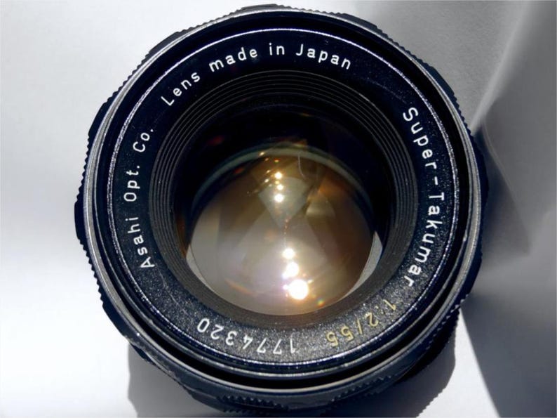 May include: A black camera lens with the text "Asahi Opt. Co. Lens made in Japan Super-Takumar 1:2/55 177320" printed around the edge.