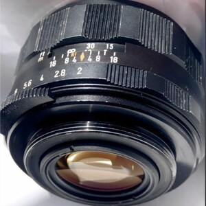 May include: A black camera lens with a silver ring and a black aperture ring. The aperture ring has markings for f/5.6, f/4, f/2.8, f/2, f/1.8, f/1.6, f/11, f/16, f/8, f/4, f/2.8, f/4, f/8, f/11, f/16, f/30, and f/15.