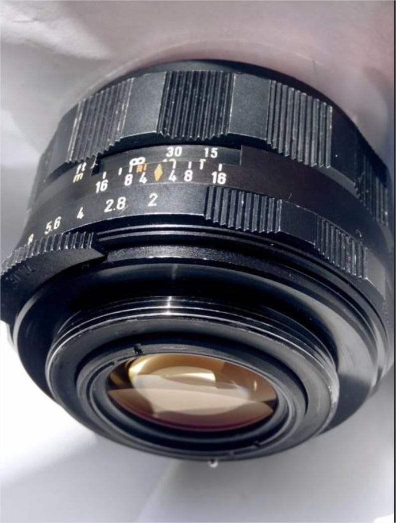 May include: A black camera lens with a silver ring and a black aperture ring. The aperture ring has markings for f/5.6, f/4, f/2.8, f/2, f/1.8, f/1.6, f/11, f/16, f/8, f/4, f/2.8, f/4, f/8, f/11, f/16, f/30, and f/15.