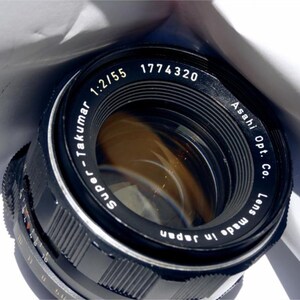 May include: A black Super-Takumar 1:2/55 1774320 lens made in Japan by Asahi Opt. Co. The lens has a silver ring around the edge and a black lens cap.
