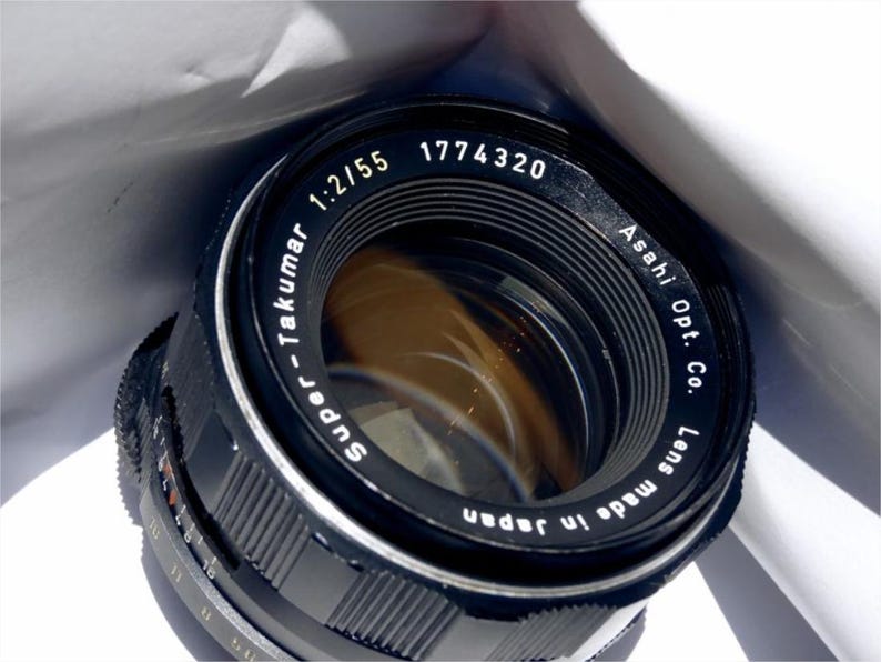 May include: A black Super-Takumar 1:2/55 1774320 lens made in Japan by Asahi Opt. Co. The lens has a silver ring around the edge and a black lens cap.