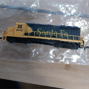 May include: A model train locomotive, featuring a yellow and black color scheme. The text "Santa Fe" is visible on the side, along with the number "3779". The model is set against a neutral background.