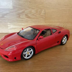 Puede incluir: Un coche modelo rojo con ruedas plateadas y un interior detallado. El coche es de estilo coupé con un diseño elegante. El coche modelo está sobre una superficie de madera.