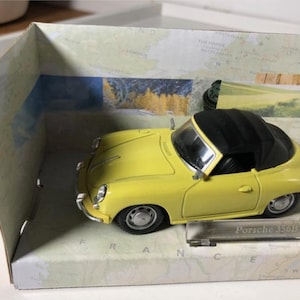 May include: A yellow Porsche 356B convertible model car with a black roof, presented in a box with a map design. The model car has detailed features and is a collectible item.