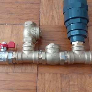 Può includere: Un sistema idraulico con quattro valvole in ottone e un filtro in plastica grigia. Le valvole hanno maniglie rosse e sono collegate da tubi. Il sistema è su una superficie in legno.