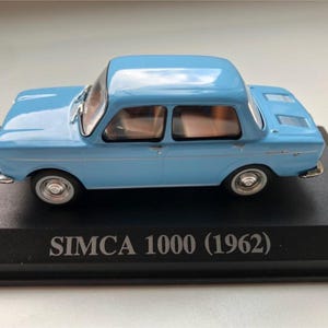 Può includere: Un'auto modello SIMCA 1000 (1962) azzurra. Il modello di auto classica è esposto su una base nera. L'auto ha un design a due porte con dettagli cromati e ruote argentate.