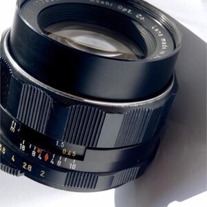 May include: A black camera lens with a silver ring and a black aperture ring. The aperture ring has markings for f/1.5, f/2, f/2.8, f/4, f/5.6, f/8, f/11, f/16, and f/0.45. The lens is labeled "Asahi Opt. Co. Lens Made in Japan".