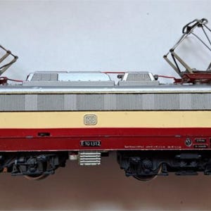 May include: A model electric train locomotive in cream, red, and silver. The train has two pantographs and the number 2 on the side. The model has the text "E10112" on the side.
