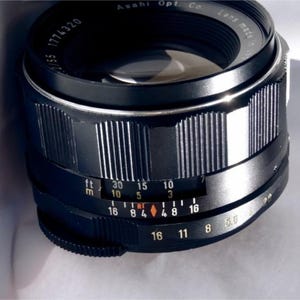 May include: A black camera lens with a silver ring and markings in feet and meters. The lens has a depth of field scale and an aperture ring.