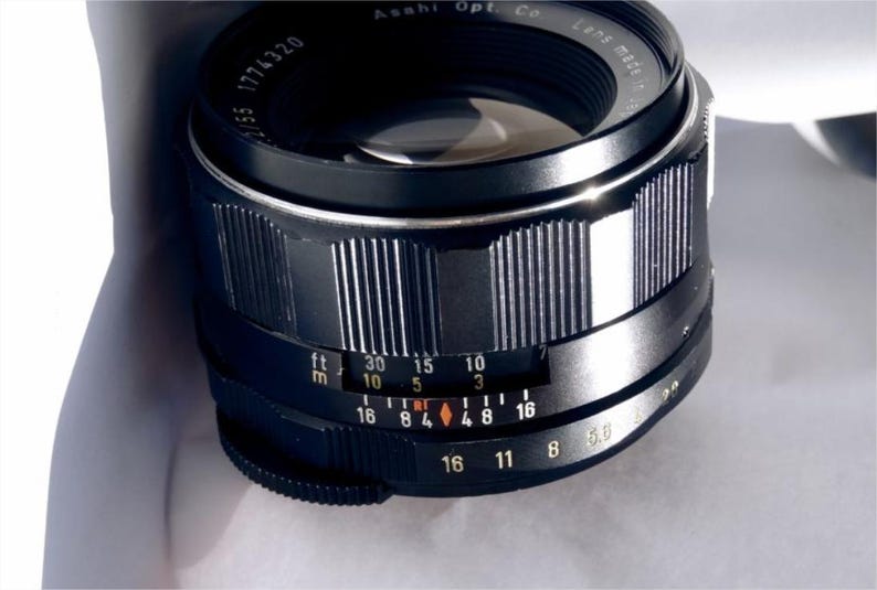 May include: A black camera lens with a silver ring and markings in feet and meters. The lens has a depth of field scale and an aperture ring.