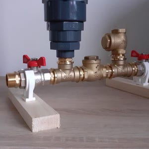 May include: A plumbing system with two brass valves and a gray filter. The valves are connected to a pipe and supported by two wooden blocks.