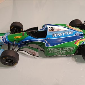 Peut inclure: Modèle réduit de voiture de course Benetton de Formule 1 verte, bleue et blanche. Le modèle a des pneus noirs et présente des logos de sponsors, dont "elf" et "Ford". La voiture est une réplique détaillée.