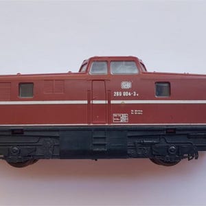 May include: A maroon and black model train locomotive. The model features a detailed design with windows, a roof, and the number "280 004-3." The train has a black undercarriage and is set against a white background.