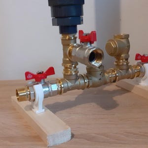 May include: A brass plumbing system with three valves and red handles. The system is mounted on two wooden blocks.