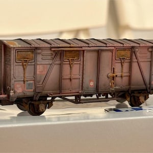 Op de afbeelding: Een verweerde modeltreinwagon in bruin- en roesttinten. De miniatuur goederenwagon heeft gedetailleerde ramen, deuren en metaalwerk, met zichtbare tekenen van slijtage. Het model staat op een spoor en toont zijn wielen en onderstel.