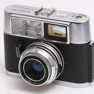 May include: A silver and black 35mm film camera with a built-in flash and a lens labeled "TETHAR 2.8/50".