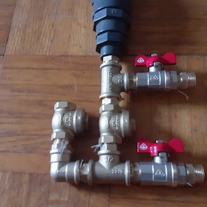 May include: A close-up of a plumbing system with three brass ball valves with red handles. The valves are connected to a gray pipe.