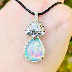 May include: A silver lotus flower pendant with a teardrop-shaped iridescent opal stone. The pendant is on a black cord.