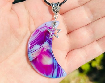 May include: A crescent moon pendant necklace made of purple and white agate with a silver star charm. The necklace has a black cord.