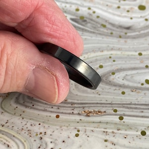 May include: A black ring with a smooth, polished finish. The ring is thin and has a simple design.