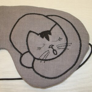 May include: Gray eye mask with a black embroidered sleeping cat design.