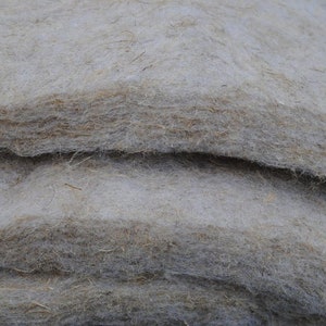 May include: Close-up of stacked, light-colored fibrous material. The layers have a soft, textured appearance with variations in color, ranging from light beige to a darker brown. The material appears to be natural and possibly used for insulation or padding.