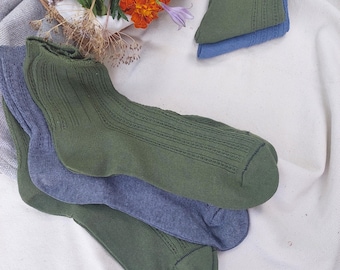 May include: A collection of ribbed socks in olive green and muted blue tones. The socks feature a delicate vertical knit pattern along the sides. Some socks are folded and stacked, displaying the textured fabric and consistent color palette.
