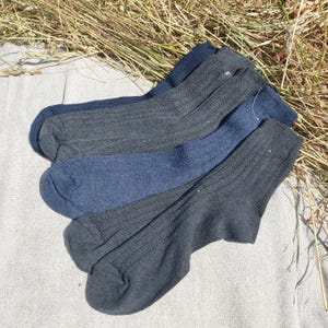 May include: A set of four ribbed socks in varying shades of dark blue, charcoal gray, and black. Each sock features a vertical ribbed texture running from the cuff down to the toe, with a standard crew length design and a consistent knit pattern.