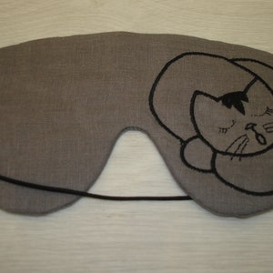 May include: Gray linen sleep mask with a black embroidered sleeping cat design.