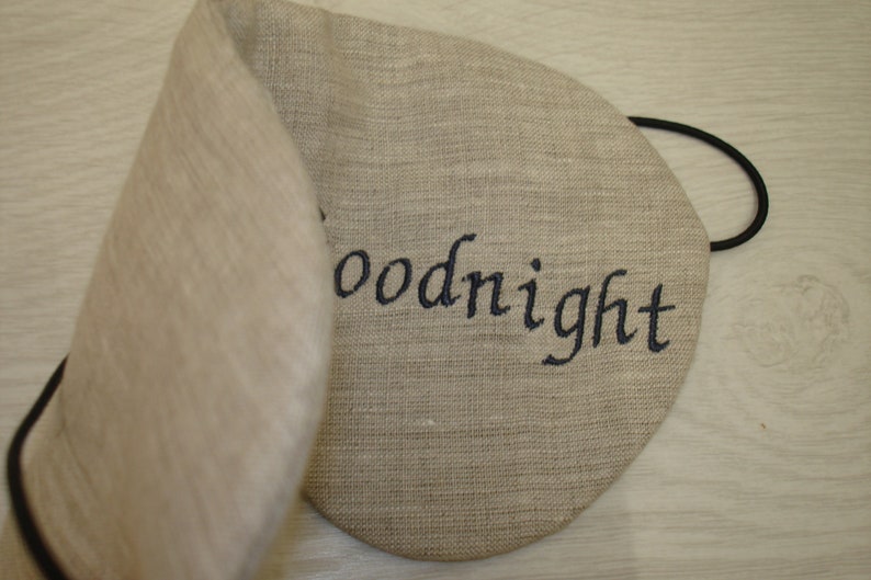 May include: A beige linen sleep mask with an elastic band and the word "goodnight" embroidered in black thread.