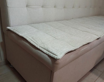 May include: A beige upholstered sofa with a tufted back and a removable cushion. The sofa has a storage compartment underneath the seat.
