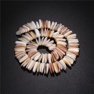 May include: A necklace made of natural shell beads. The beads are elongated and vary in color from white to light orange. The necklace is arranged in a circular pattern against a black background.