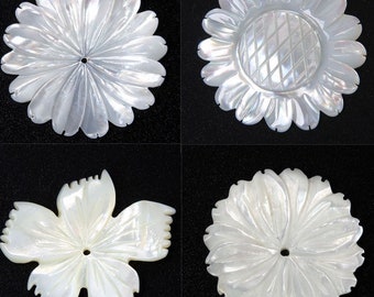 May include: Four white mother-of-pearl flower-shaped pendants. Each pendant has a different design, including a sunflower and a multi-petal flower. The pendants have a hole for stringing and are set against a black background.