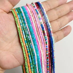 Puede incluir: Una colección de cuentas finas de forma cuadrada dispuestas en múltiples hilos verticales. Las cuentas presentan un espectro de colores vibrantes que incluye naranja, verde, turquesa, rosa, blanco, rojo, azul y negro, creando un conjunto multicolor.