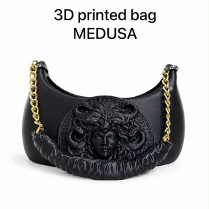 以下が含まれることがあります： 「3D printed bag MEDUSA」というテキストが記載された黒い3Dプリントバッグ。バッグは三日月型で、中央にメデューサの頭部のレリーフがあり、黒い質感のあるハンドルが両側の金色の金属チェーンに取り付けられています。