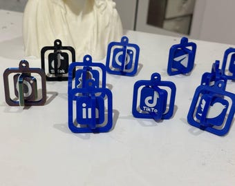 Op de afbeelding: Een verzameling blauwe en zwarte sleutelhangers met verschillende social media logo's, waaronder Instagram, TikTok, Twitter, Facebook en LinkedIn. De sleutelhangers zijn gemaakt van plastic en hebben een 3D-ontwerp.