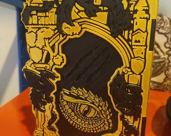 May include: A gold and black fantasy-themed decorative panel featuring a dragon eye, castles, and dragons. The panel has a layered design with intricate details and a textured appearance. The overall theme is medieval fantasy.