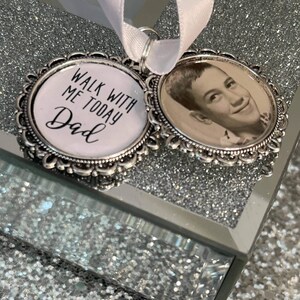 May include: Two silver-toned memorial charms with a white ribbon. One charm features a black and white photo of a young man. The other charm has the text "Walk with me today Dad".