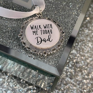 May include: A silver charm with a white background and black text that reads "Walk with me today Dad". The charm is attached to a white ribbon.