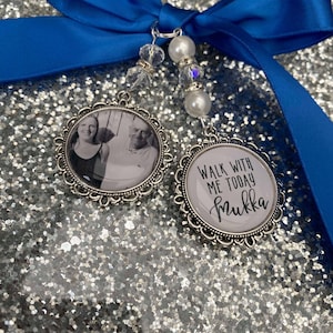 Puede incluir: Dos dijes de foto plateados con una cinta azul. Un dije presenta una foto de dos personas, y el otro dije tiene el texto "Walk with me today" y la palabra "mukka".