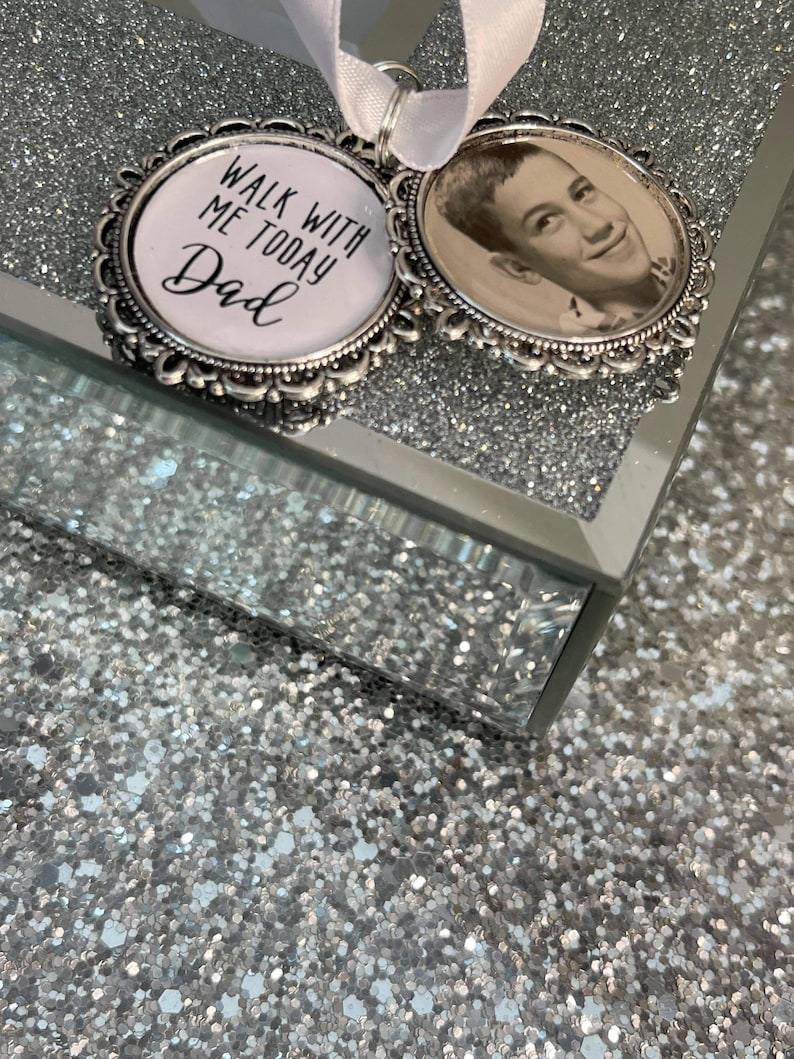 May include: Two silver-toned memorial charms with a white ribbon. One charm features a black and white photo of a young man. The other charm has the text "Walk with me today Dad".