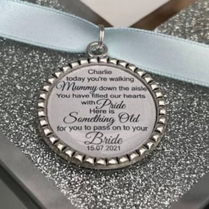 Peut inclure: Un charme argenté avec un fond blanc et du texte noir qui dit "Charlie aujourd'hui tu marches Maman dans l'allée Tu as rempli nos cœurs de fierté Voici quelque chose de vieux pour toi à transmettre à ta Mariée 15.07.2021".