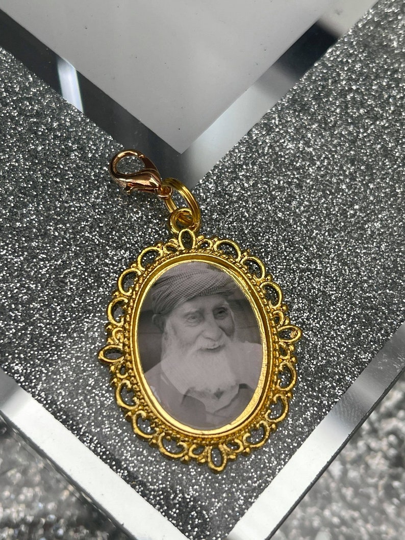 May include: Gold-toned metal charm with a black and white photo of a man with a beard and a hat inside a decorative oval frame.