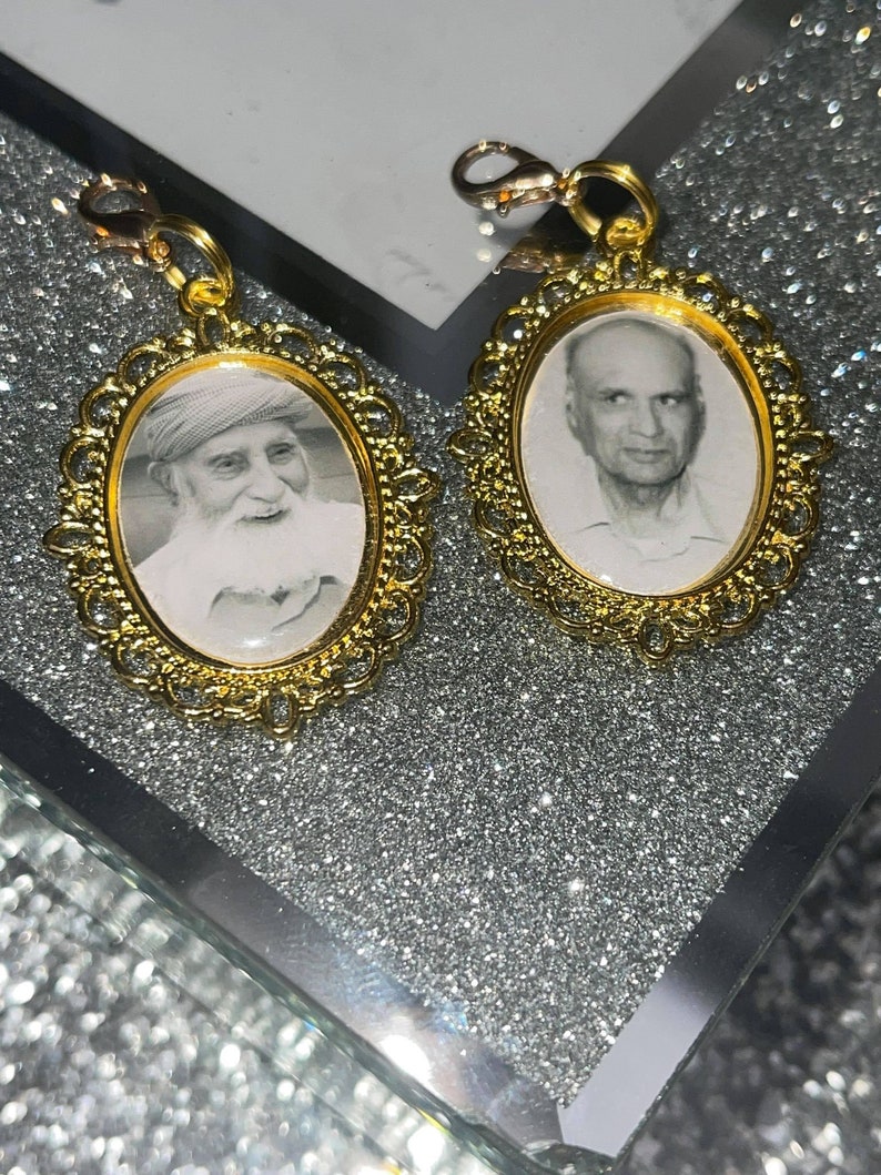 May include: Two gold-toned oval picture frames with ornate edges, each containing a black and white photo of an older man. The frames are attached to gold-toned chains.