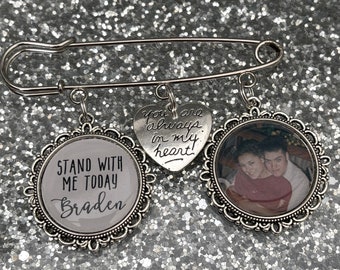 May include: A silver safety pin with three charms. One charm is a heart with the text "You are always in my heart!" The second charm is a round picture frame with a photo of a couple. The third charm is a round frame with the text "Stand with me today Braden".