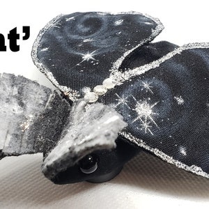 May include: A black fabric bat with silver glitter accents and a starry night sky design. The bat has a small black head with a single black eye. The text 'Night' is visible in the image.