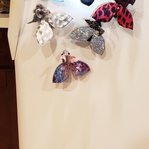 May include: A white refrigerator door with eight colorful butterfly magnets attached. The butterflies are made of fabric and have different patterns and textures.