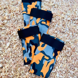 May include: Four orange, gray, and black camouflage dog booties with black elastic straps.