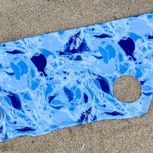 May include: A blue and white marbled fabric with two cut-out circles. The fabric has a swirling pattern reminiscent of water.